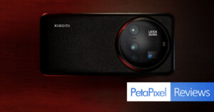 A smartphone with a large circular Leica camera module is placed on a textured surface. The phone's brand logo is visible. At the bottom right, there are graphics displaying "PetaPixel Reviews" with blue and white backgrounds.