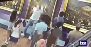 Surveillance footage shows several people viewing paintings in an art gallery. One person appears to be touching or pointing at a painting. The image has a TGR logo in the bottom right corner. Faces are blurred for privacy.